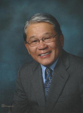 william t fujioka headshot, he is wearing a grey suit with a blue grey background